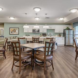 A modern kitchen and dining area with wooden tables and chairs, featuring contemporary lighting fixtures and a bright atmosphere.