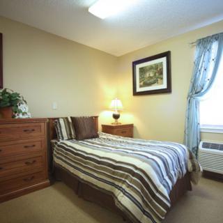 A cozy bedroom featuring a neatly made bed with striped bedding, wooden furniture, and soft lighting.