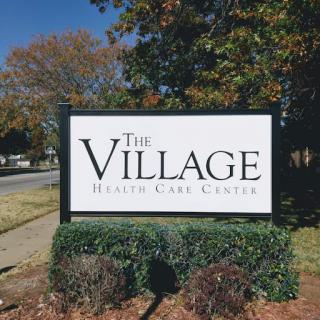 Sign for The Village Health Care Center, showcasing outdoor landscaping.