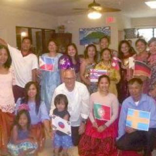 A group of people dressed in cultural attire holding various national flags, gathered indoors for a celebration.