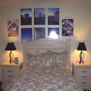 A cozy bedroom with a large bed, flanked by two nightstands and lamps, and decorated with wall art above the headboard.