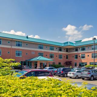A modern hotel with a welcoming entrance surrounded by a parking lot and a clear blue sky.