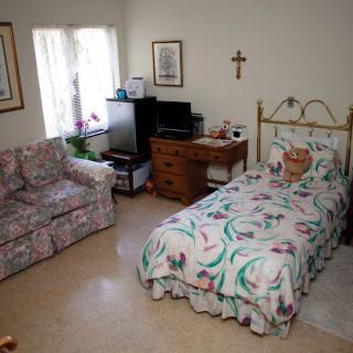 A cozy bedroom with a single bed, floral bedding, and a small sofa alongside a television and dresser.