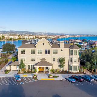 Aerial view of a waterfront building with nearby parking and harbor scenery.