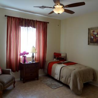 A cozy bedroom with a single bed, rust-colored curtains, and a ceiling fan.