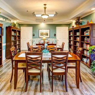 A cozy library room with wooden tables and chairs surrounded by bookshelves.