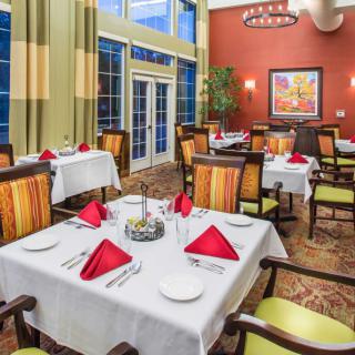 Elegant dining area with tables set for guests, featuring red napkins and comfortable seating.