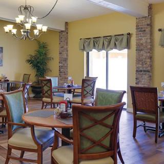 A cozy dining area with wooden tables and chairs, lit by a chandelier and natural light.
