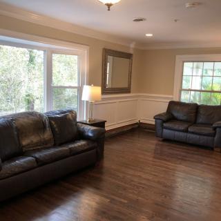 A cozy living room with leather sofas, a standing lamp, and large windows letting in natural light.
