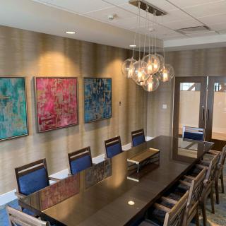 A modern conference room featuring a sleek meeting table, comfortable chairs, abstract artwork on the walls, and a stylish chandelier.