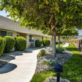 A winding pathway lined with trees and bushes leads to a building.