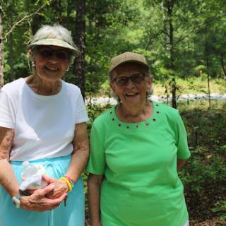 Two smiling elderly women enjoying a sunny day in nature.