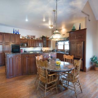 A spacious kitchen with wooden cabinets, a dining table with chairs, pendant lighting, and hardwood flooring.