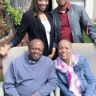A happy family posing together outdoors, with two seated in front and two standing behind.