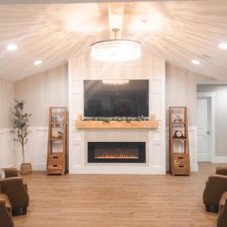 A modern living room with a cozy fireplace and mounted TV, featuring minimalist decor and wood flooring.