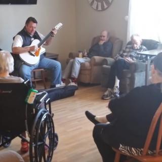 A musician playing guitar for an audience in a nursing home.