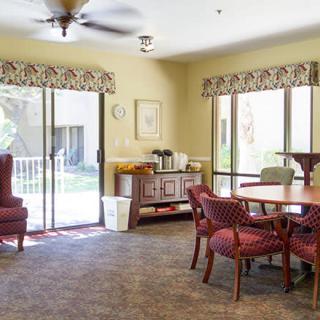 A cozy living room with a table, chairs, and large windows overlooking a garden.