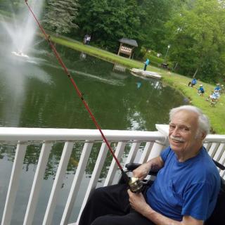 An elderly man fishing by a pond on a peaceful day.