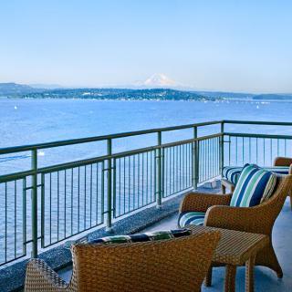 A balcony with comfortable seating offers a stunning view of the ocean and a distant mountain.