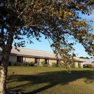 A scenic view of a building with a tree casting a shadow on the lawn.