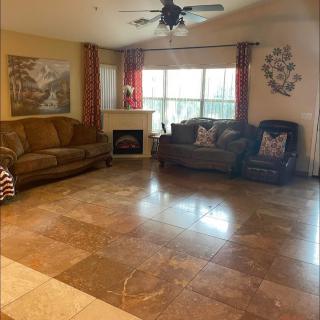A spacious living room with tile flooring, featuring two sofas, a ceiling fan, and a large window with curtains.