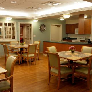 A cozy dining room with tables and chairs, featuring a kitchen area and warm lighting.