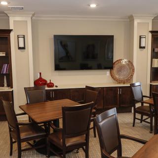A conference room with a large TV, surrounded by tables and chairs, featuring bookshelves and decorative elements.