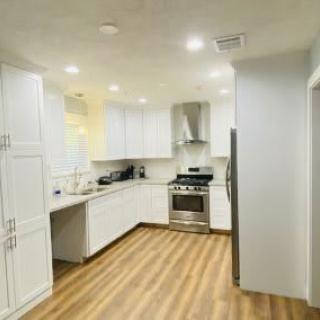 A modern kitchen with white cabinetry and wood flooring, featuring stainless steel appliances.