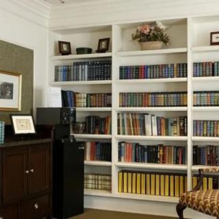 A cozy home library with a white bookshelf filled with various books and decorative items.