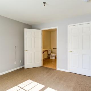An empty bedroom with carpet flooring, featuring a closet and an open door leading to a bathroom.