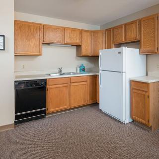 An apartment kitchen with wooden cabinets, a refrigerator, and a stove.