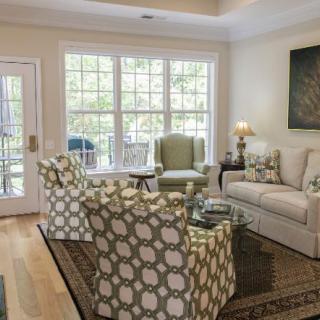 A cozy living room with patterned chairs, a comfortable sofa, and large windows letting in natural light.