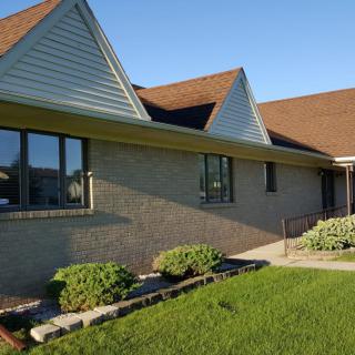 A brick residential house with a triangular roof, windows, and a neatly maintained yard.