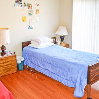 A neatly arranged bedroom with a single bed, blue bedspread, and wooden furniture.