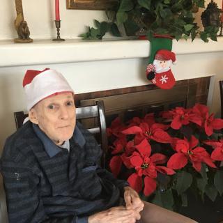 An elderly person wearing a Santa hat, surrounded by festive poinsettias, celebrating the holiday spirit.