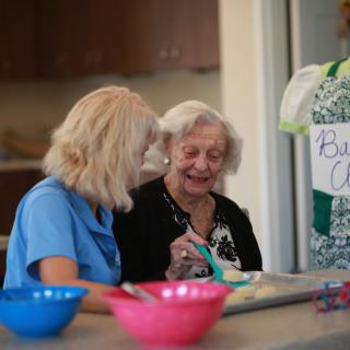Two elderly women enjoying a conversation while baking together in a kitchen.