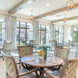 A bright and elegant dining room with neatly arranged tables and chairs, large windows, and stylish lighting.