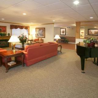 A spacious and warmly decorated living room featuring a red sofa, a black piano, and various furnishings including lamps and framed artwork.