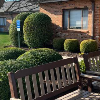 A well-maintained garden area with benches and neatly trimmed bushes in front of a brick building.