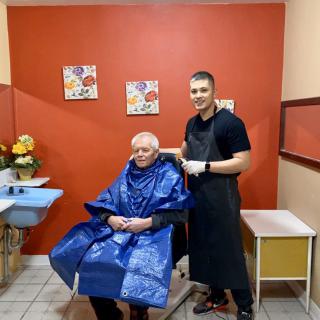 A young barber giving a haircut to an elderly person in a barbershop.