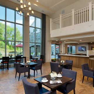A modern restaurant dining area with large windows, offering an inviting ambiance with wooden floors and a chandelier.