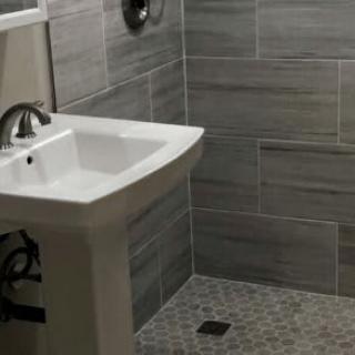 A modern bathroom with a pedestal sink and tiled shower area.