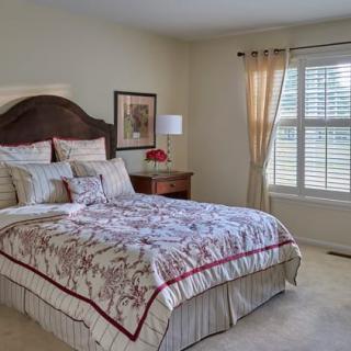 A cozy bedroom with a neatly made bed, decorative pillows, and natural light coming through the window.