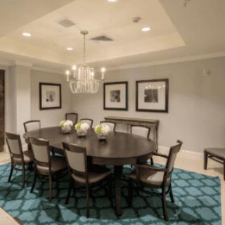 A well-appointed dining room featuring a large round table, surrounded by chairs, with a chandelier overhead and artwork on the walls.