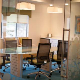 A modern conference room with a glass table, office chairs, and a well-lit atmosphere.