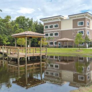 A tranquil pond with a wooden gazebo, reflecting the adjacent building and lush surroundings.