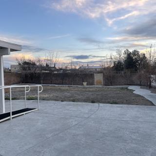 A serene outdoor space featuring a concrete patio, expansive grass area, and a beautiful sky with scattered clouds.