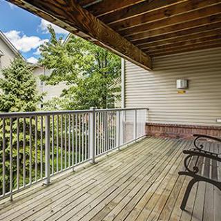 A spacious wooden balcony with outdoor seating, overlooking trees in a residential area.