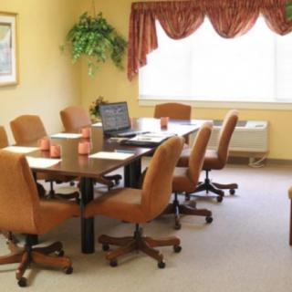 A conference room with a long meeting table and office chairs, featuring a laptop and decorative elements.
