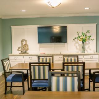 A modern dining room with striped chairs, a wall-mounted TV, and a decorative vase with flowers.